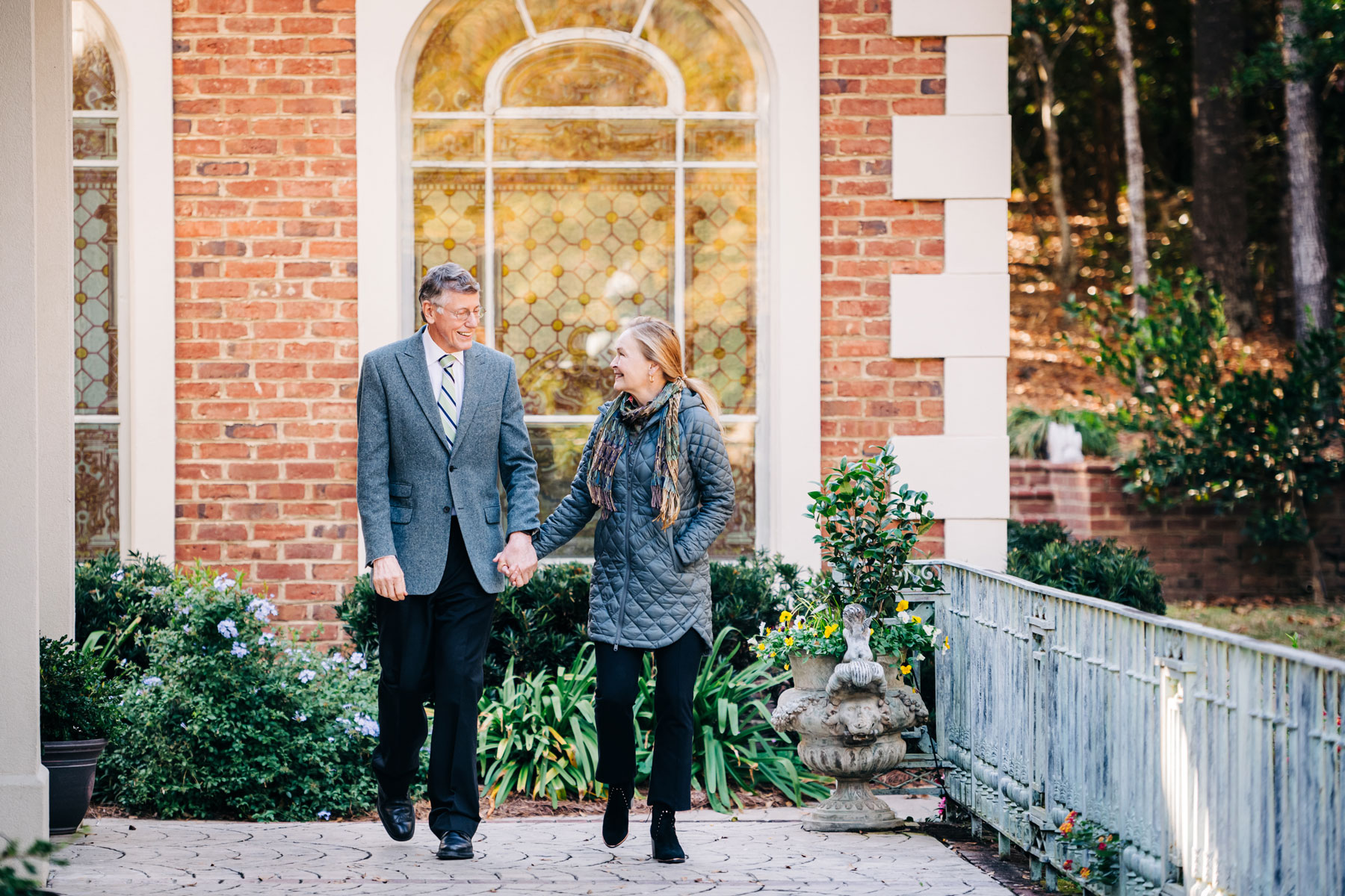 Marnix and Mary Heersink smile at each other as they walk hand-in-hand outside a large brick home.