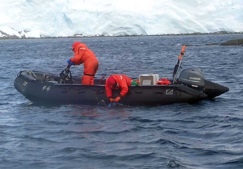 Two people in Zodiac boat helping divers get their gear into the boat.