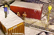 Photo by Joanna Hubbard. Two women, dressed in their hard hats and other cargo handler garb, waved white handkerchiefs from atop and beside a cargo container on the edge of the pier.  

