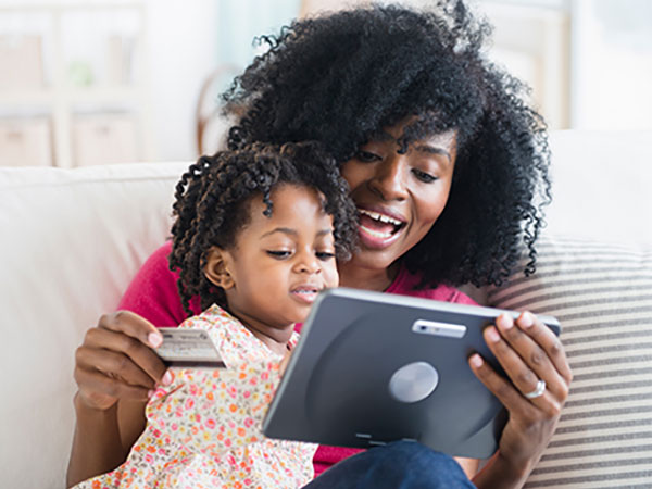 Smiling woman shopping on her tablet while her child watches. 