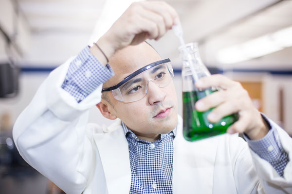 Man in lab coat using beaker.