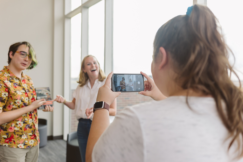 Two graduate students pose as another student records them with a smartphone
