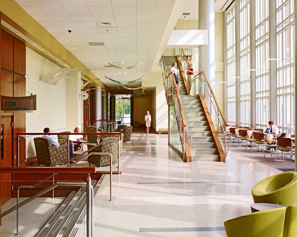 Interior photo of heritage hall showing a staircase and students conversing in lounge chairs.