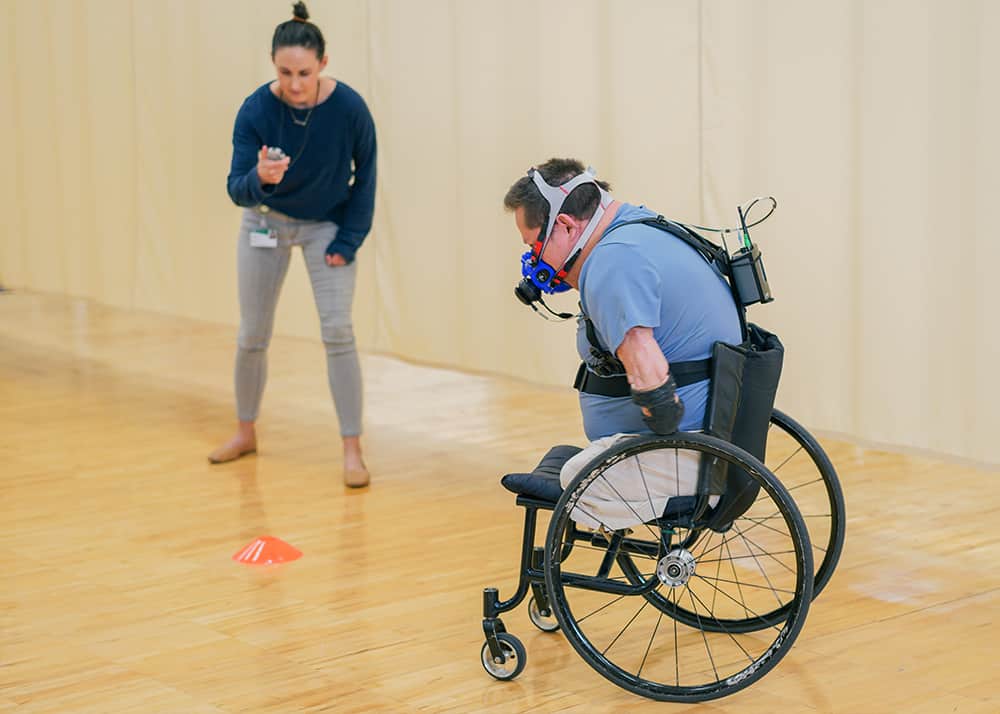 Patient wearing the COSMED K5 running a course in his wheelchair while being timed by an observer. 