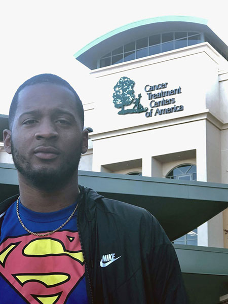 Rashad Hayes wearing a Superman shirt and standing outside of a cancer treatment center.