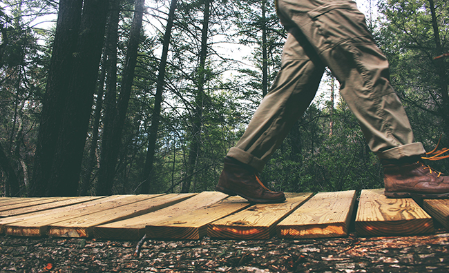 Legs of a person walking on a suspended wood bridge in the forest