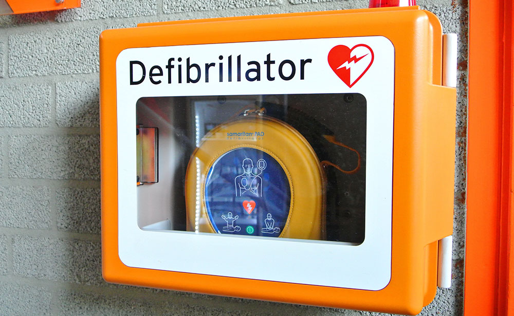 Defibrillator in an orange and white box mounted on a wall. 