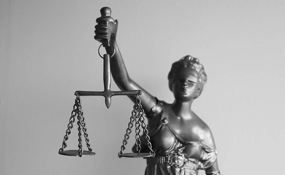 Statue of Lady Justice, blindfolded and holding up scales. Image is black and white.