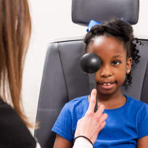 Child sitting in examination chair with optometrist holding a black plastic piece to her eye