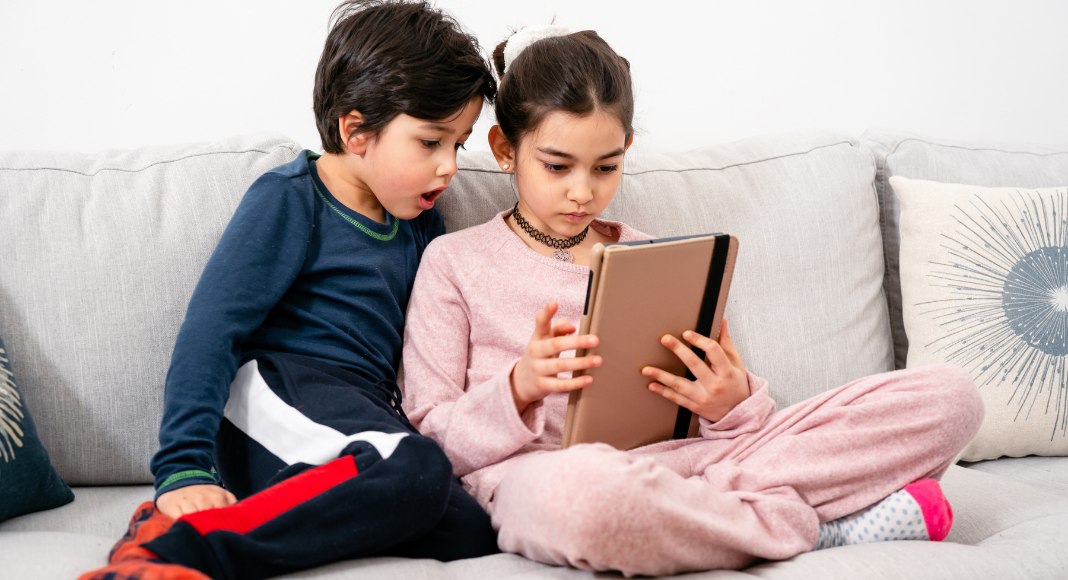 A brother and sister sitting on the couch playing on an iPad