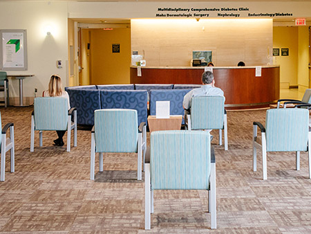 Back, two patients are sitting in chairs spread apart for COVID-19 (Coronavirus Disease) social distancing in the waiting area of a medical office in the Kirklin Clinic, May 2020.a