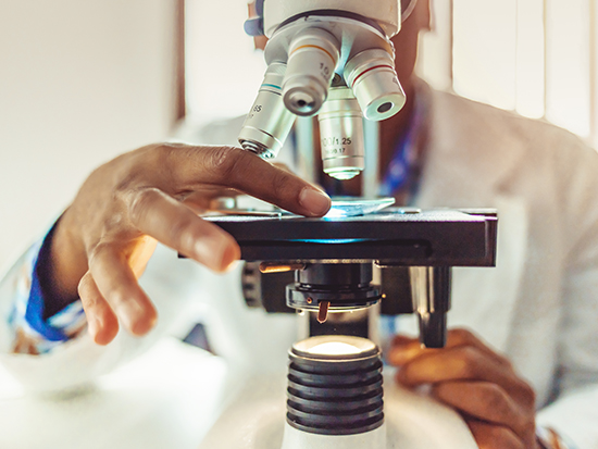 African-American men in a laboratory microscope with microscope slide in hand.