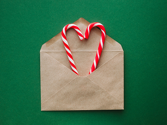 Candy canes in shape of heart in envelope over emerald green background. Christmas greeting card.