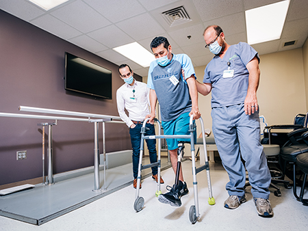 Brian Mueller, certified prosthetist and manager of the UAB Orthotics and Prosthetics Clinic, assists Vasquez in his first steps since the accident. 