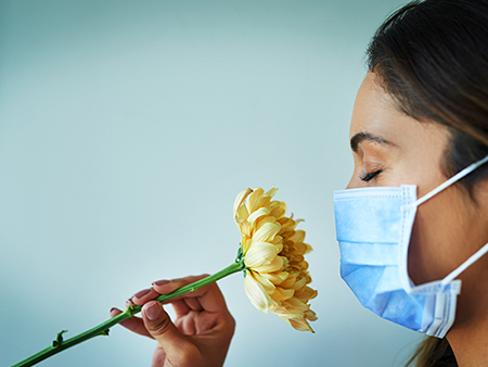 Shot of a young woman smelling a flower while wearing a surgical mask