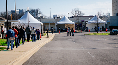 Overall of people standing in line near white tents at the UAB COVID-19 Vaccination Site at Parker High School on February 10, 2021. 