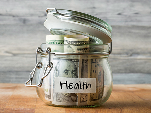Dollar bills in glass jar isolated on wooden background. Saving money for health.