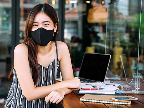 Young 20s Asian woman looking at camera while wearing a protective mask with laptop, mobile phone, and notebook for working outside in casual dress. Corona Virus - Covid 19 work online concept.