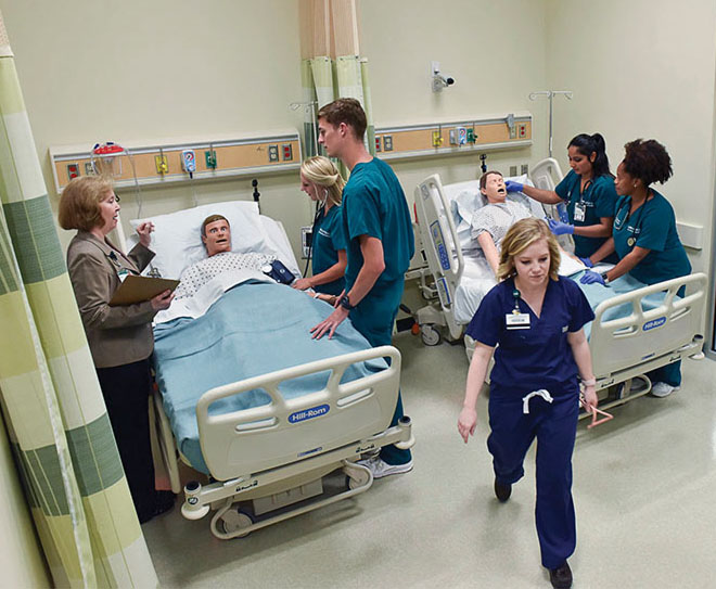 Photo of students working with simulated patients in mockup hospital room