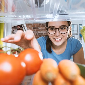 Student reaching into refrigerator packed with vegetables.