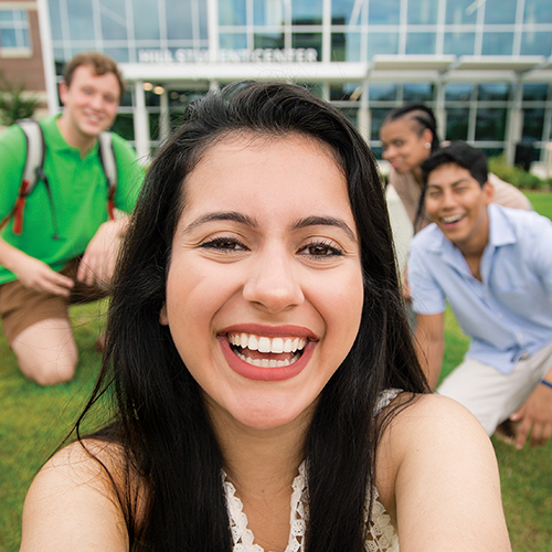 Close up of female student with diverse group of students out of focus behind her.