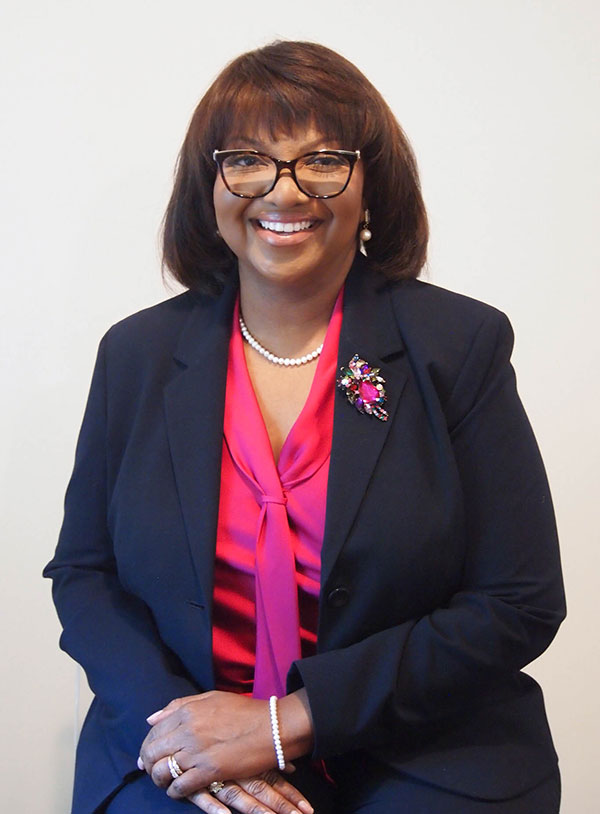 Alesia Jones is a Black woman with a big smile, wearing a navy jacket and hot pink blouse and brooch. 