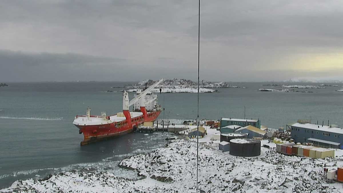 Screen grab of a webcam showing a very large red ship tied up to a very small pier