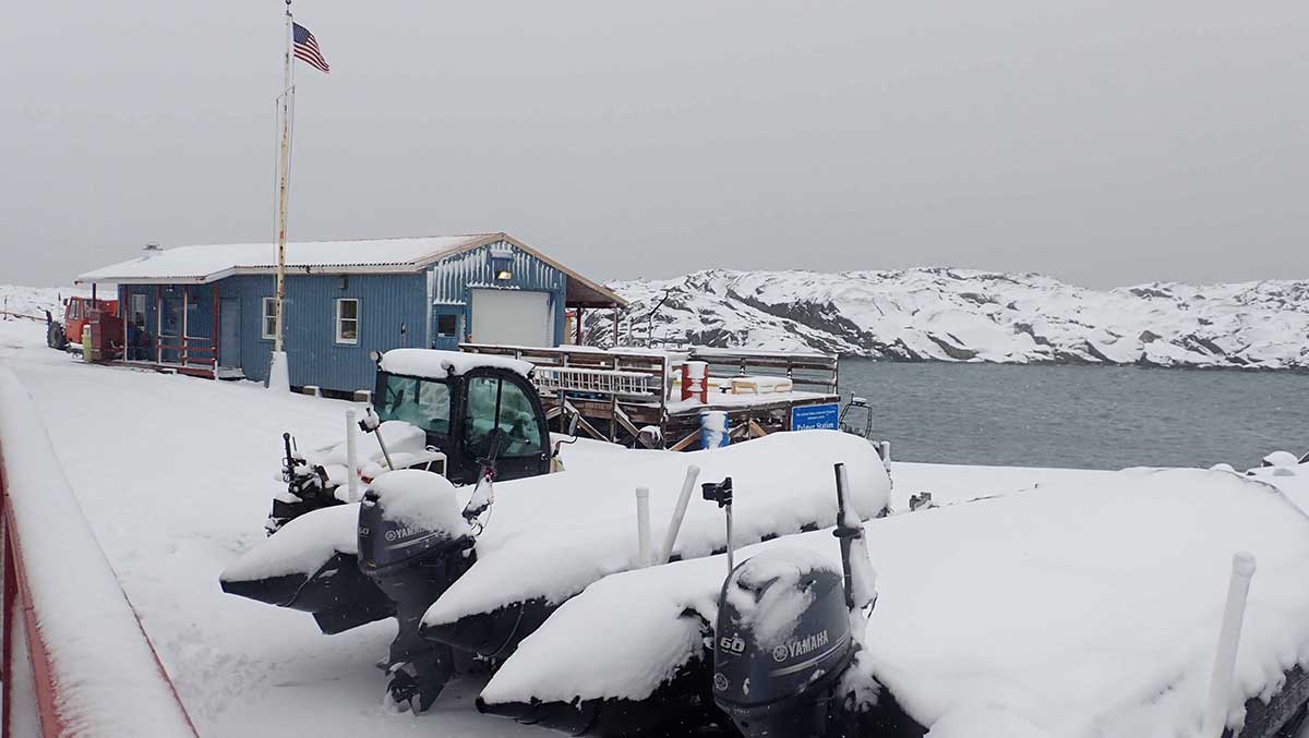 Wintry image of Palmer Station boat house and zodiacs on trailers covered with freshly fallen snow under a gray sky