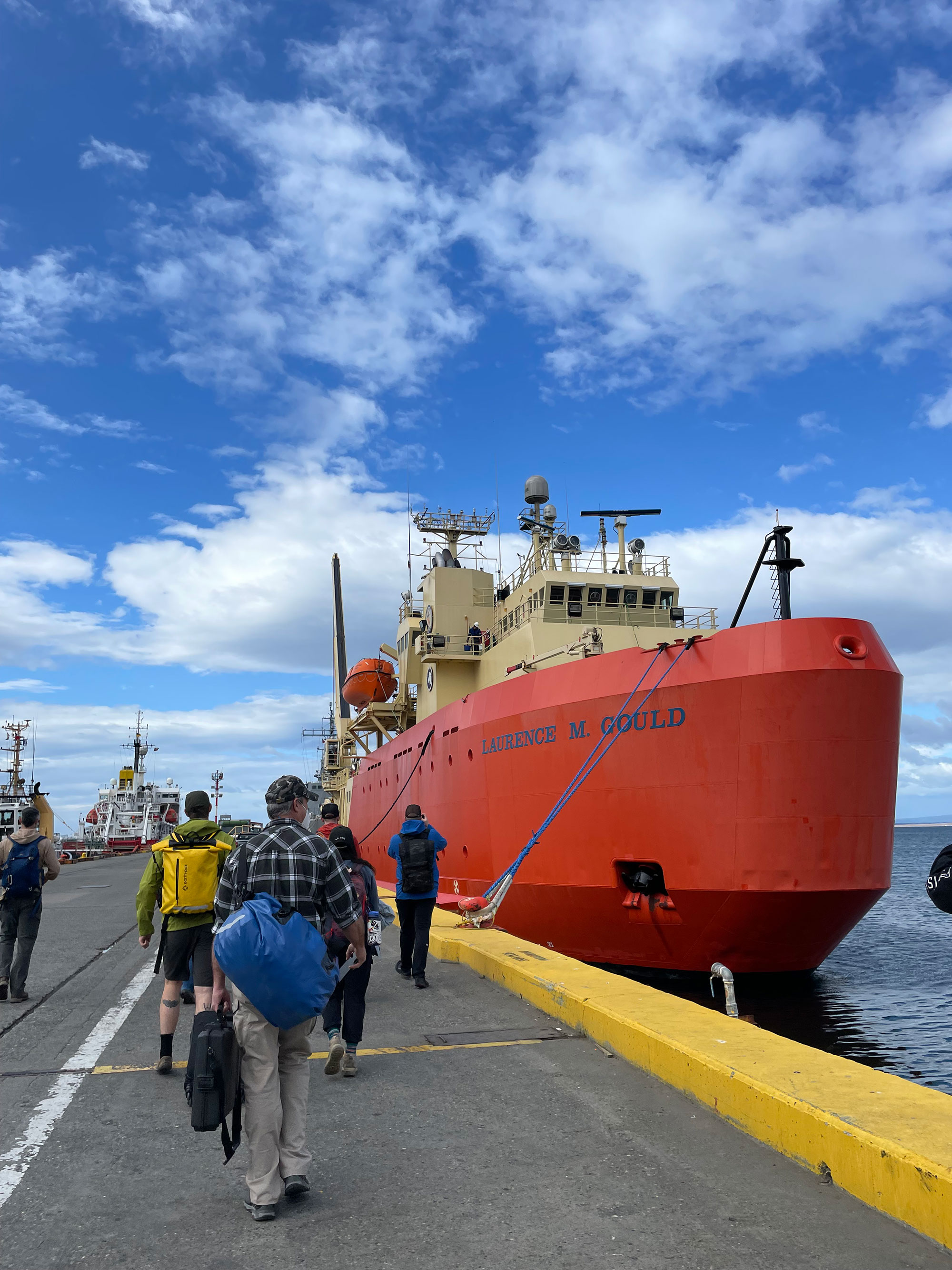 Crew walking to the Laurence M. Gould at dock - ship has a orange hull and tan structures. 