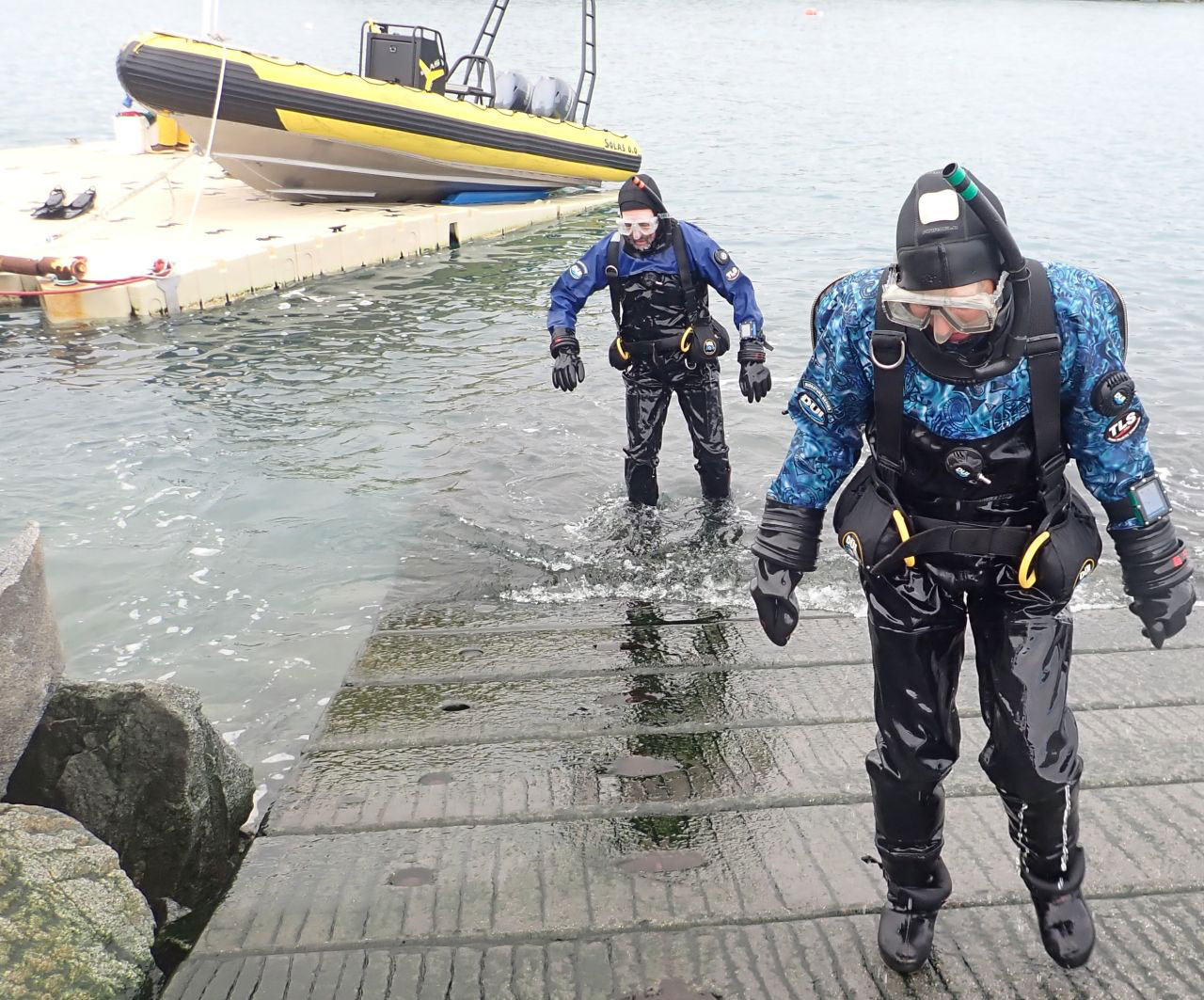 Maggie and Chuck emerging from the water after their dive, walking up a cement dock ramp. 