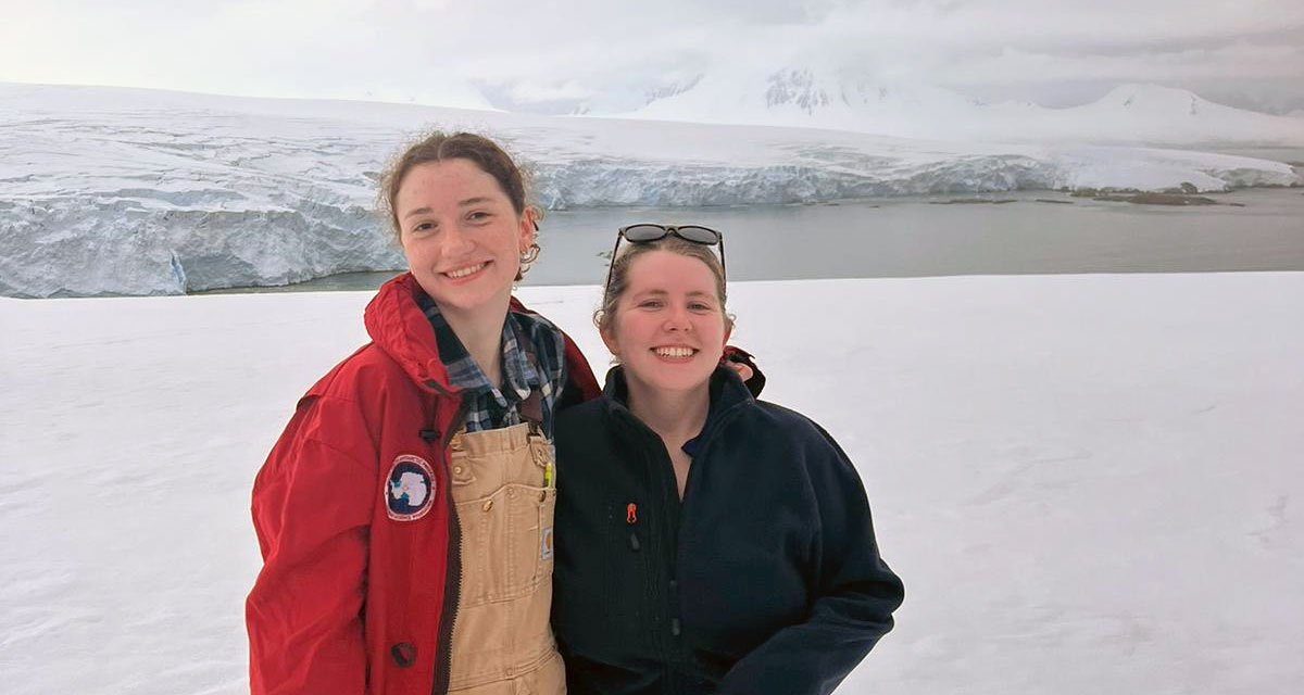 Hannah and Addie pose -- there is open water and then more glacier behind them. 
