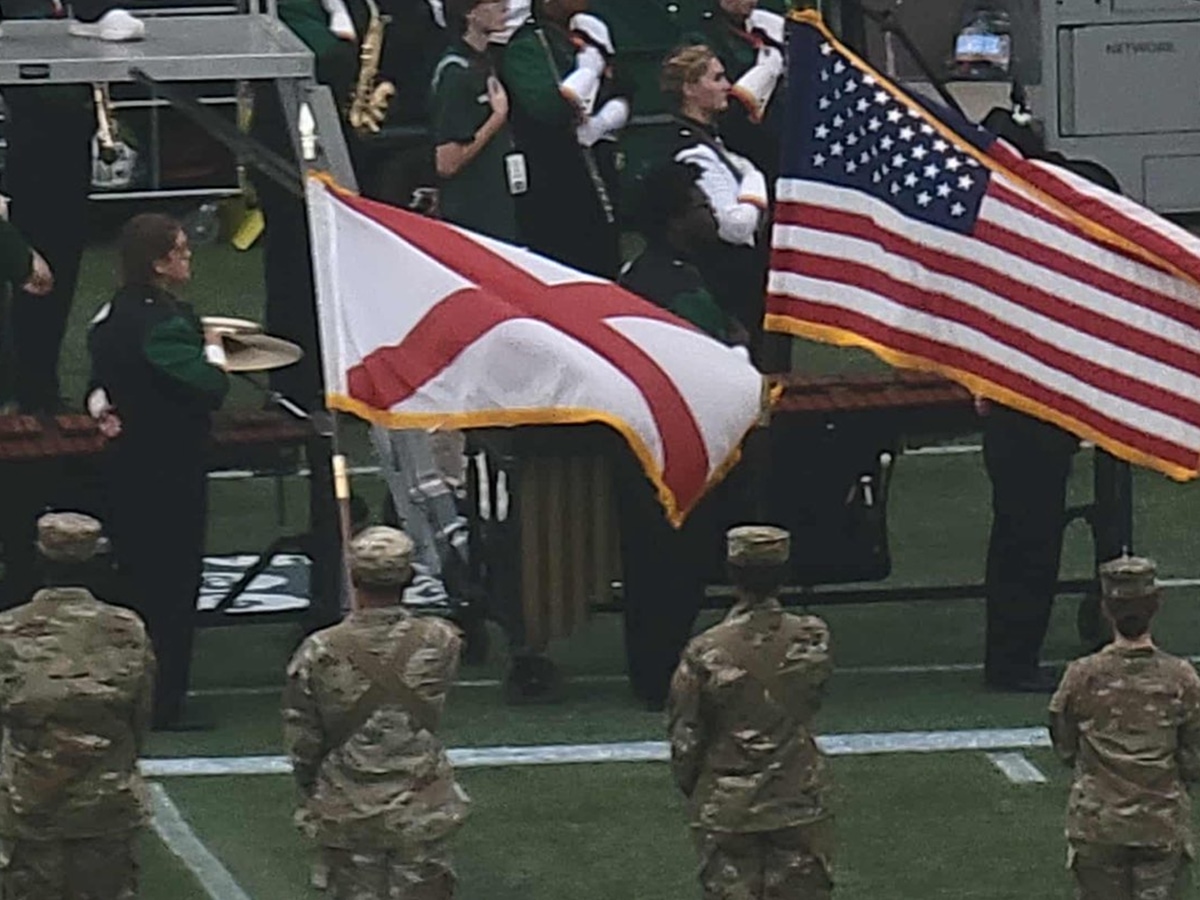 Scholars at attention holding the Alabama and US flags at an event.