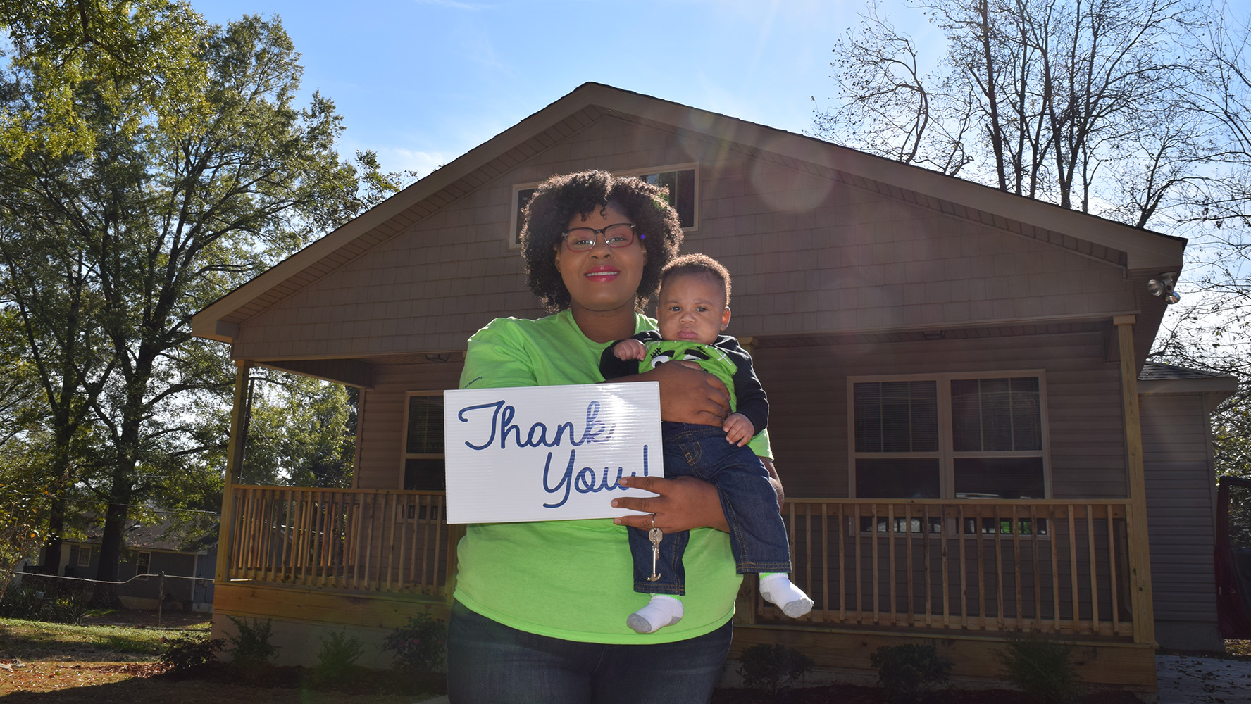 Woman and her toddler standing in front of a newly built Habitat home.