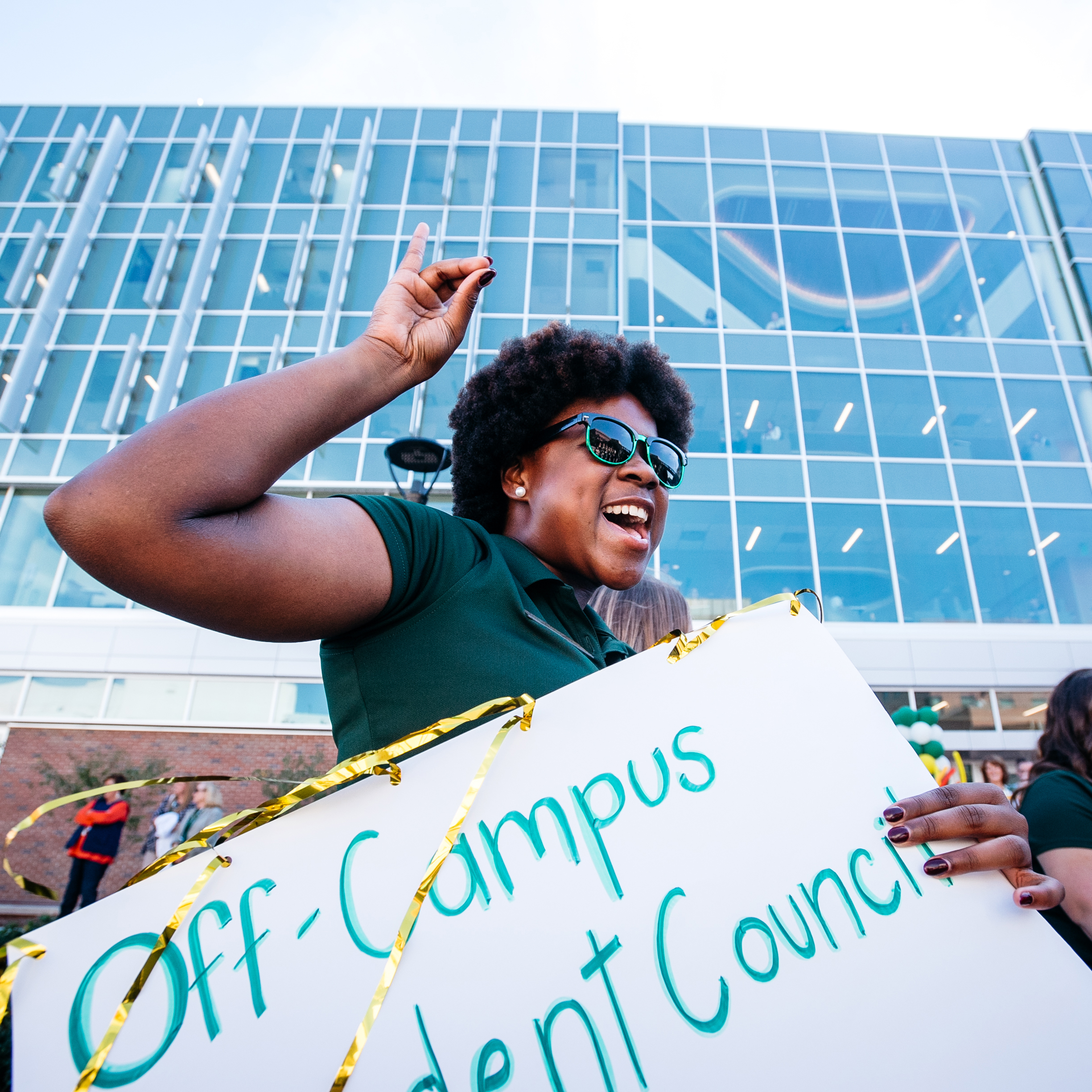 UAB student flashing the "Blaze handsign" while holding a sign stating "Off Campus Student Council"