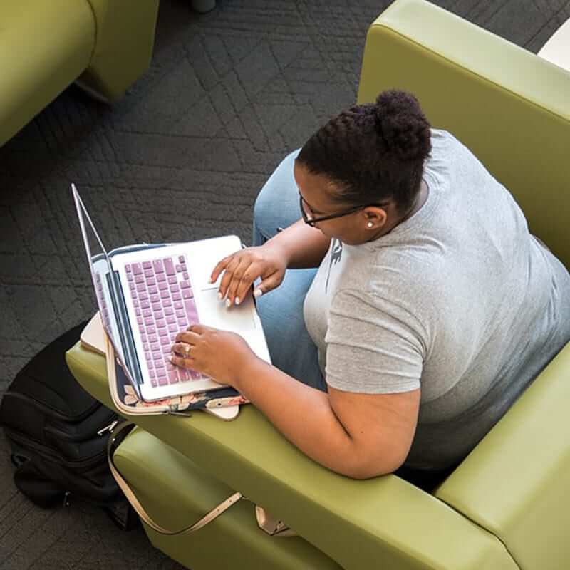 Student working on her laptop, sitting in a comfy green chair. 