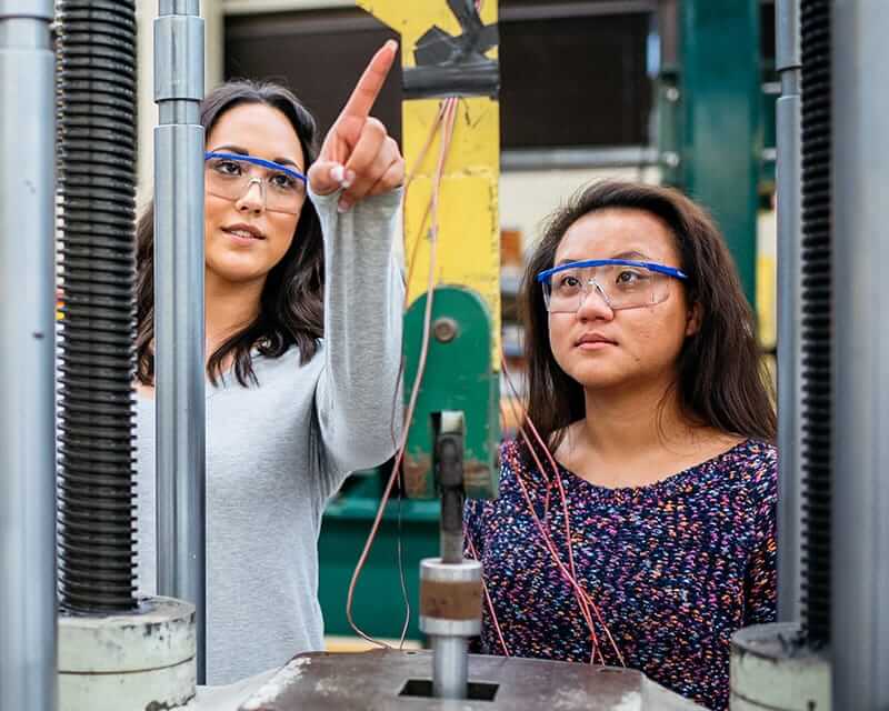 A female faculty member instructing a female student in an engineering lab. 