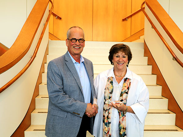 two people in front of a staircase shaking hands and smiling. One has a crystal award in hand.