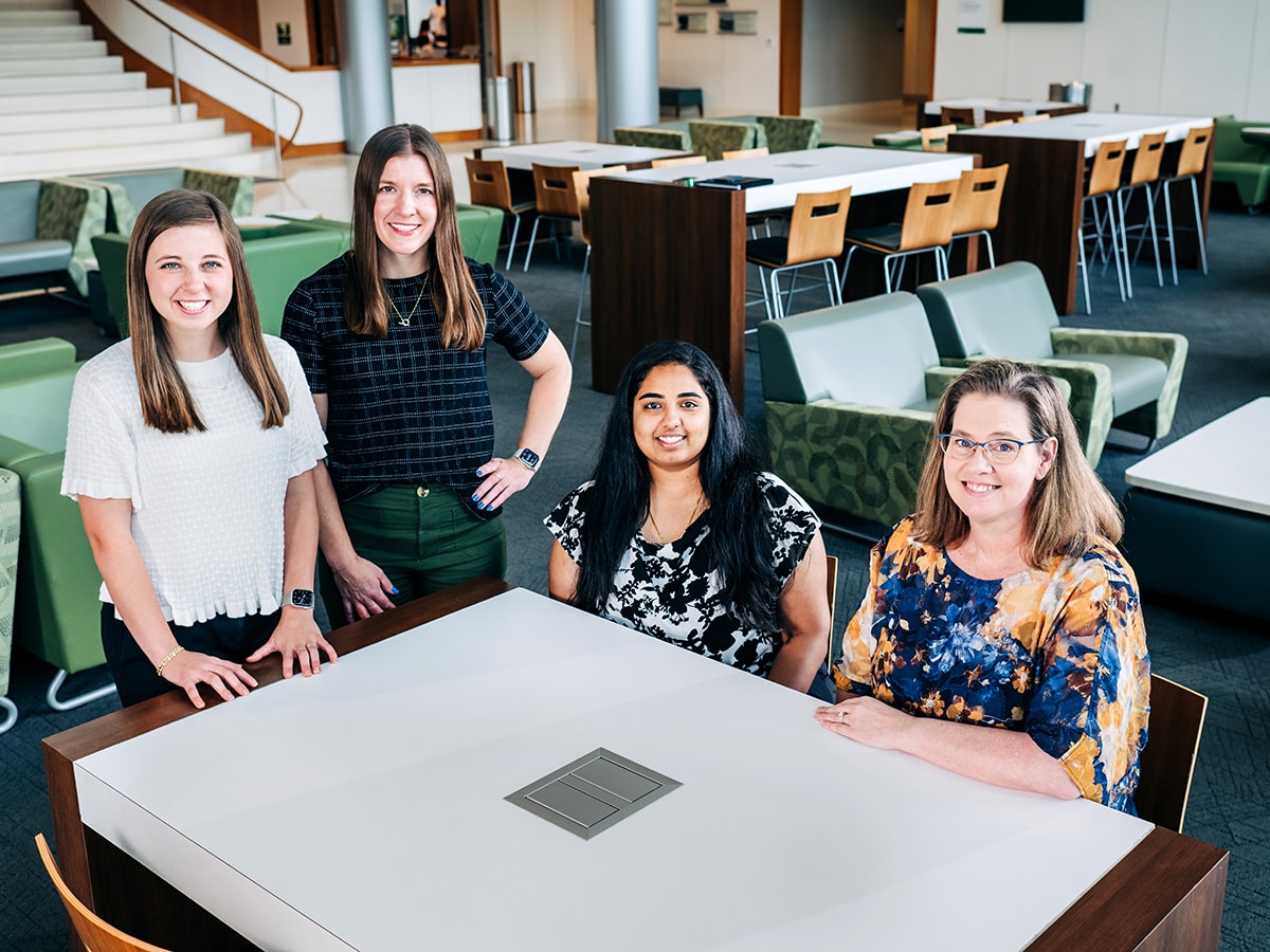 Four staff members stand or sit around a white table in a large room