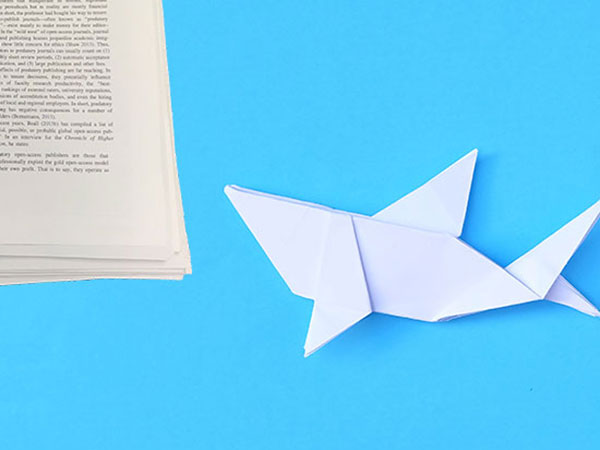 A white folded paper shark pointed toward a stack of papers. 