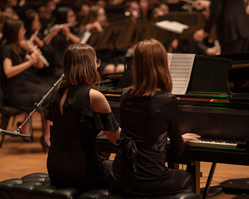 Two girls playing piano together during a concert