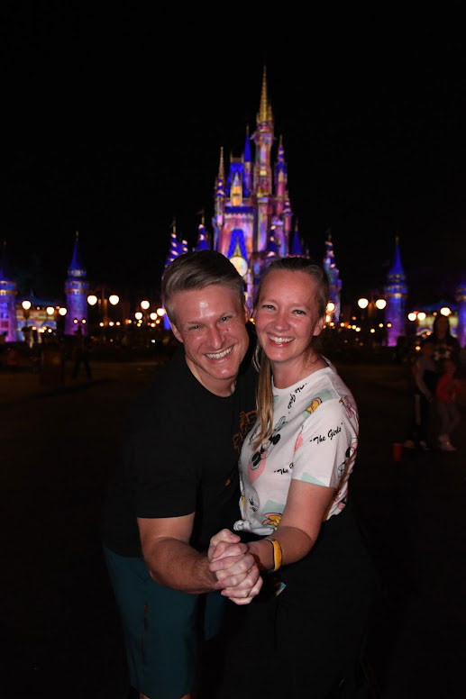 Adam and Dixie Aldrich holding hands in front of the Disney castle at night. 