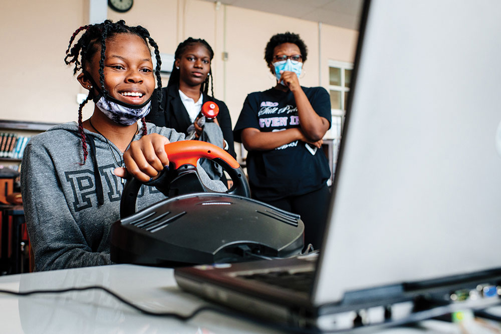 A black female highschool student with braids tests the driving simultor.