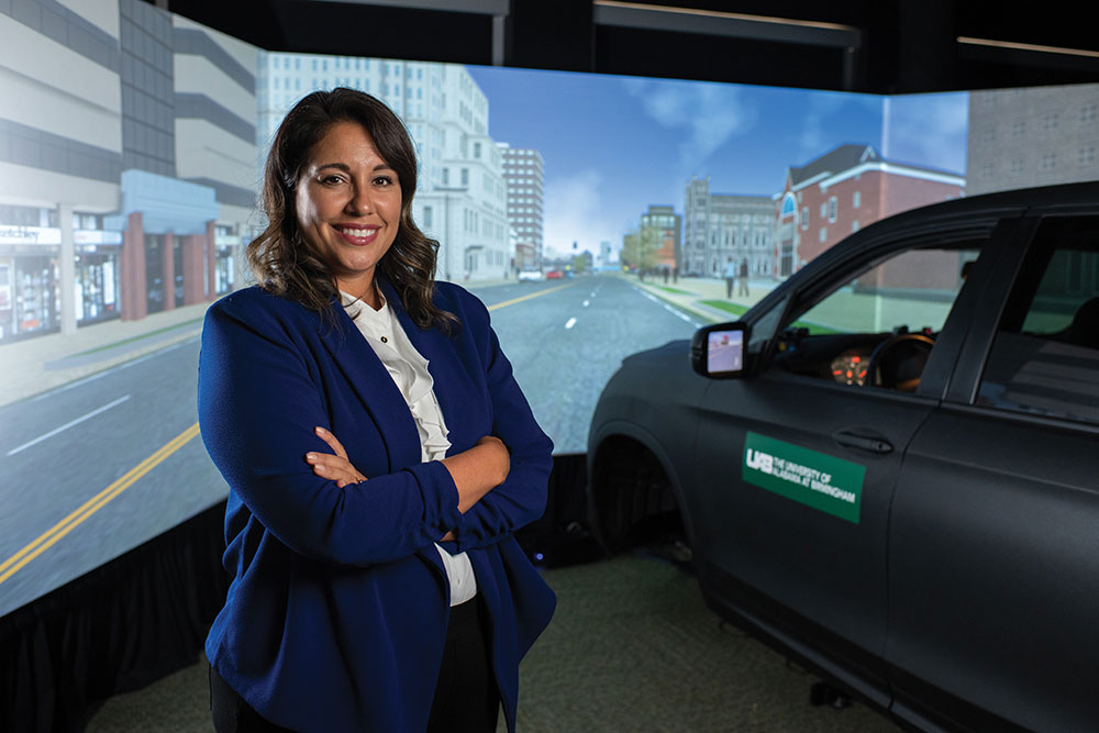A Dr. Stavrinos standing in near the car and screens of the simulator. 