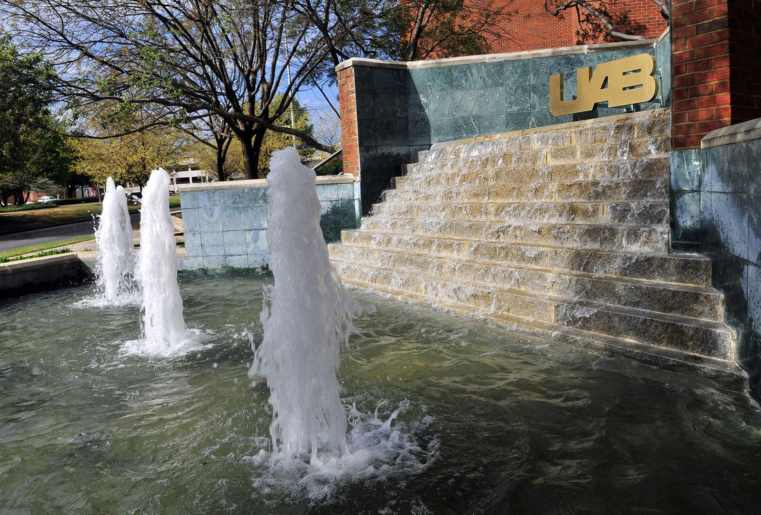 A fountain with water cascading down stairs into a pool with three water plumes spashing upwards outside of UAB's Campbell Hall.