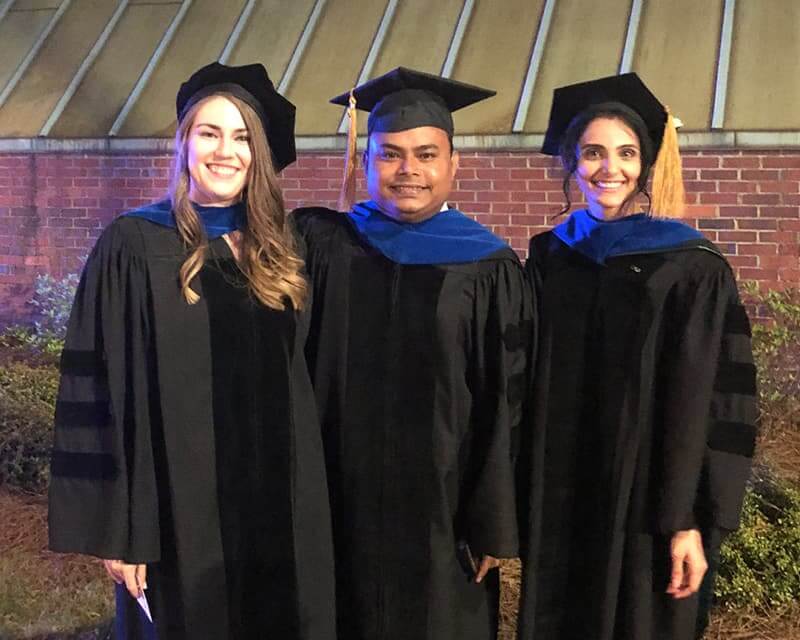 Three UAB PhD students in their caps, gowns, and hoods, smiling at graduation.