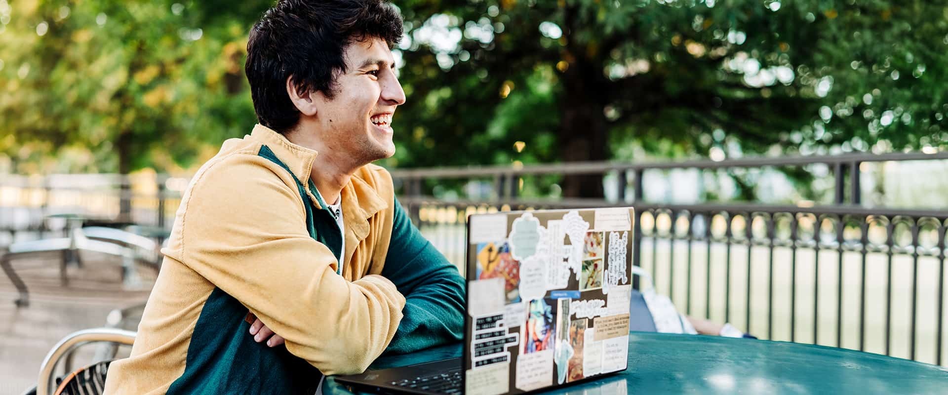 A smiling student with a laptop sitting at a table.