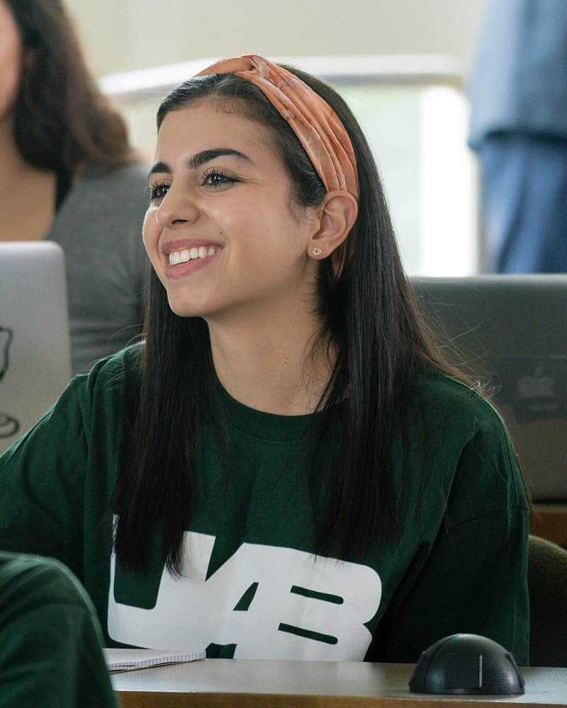 Smiling female student with olive skin, long black hair in an orange headband, and a UAB sweatshirt.