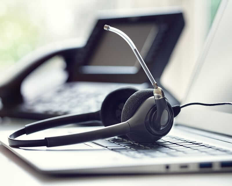 Closeup of a headset resting on a laptop, with an office phone in the background. 