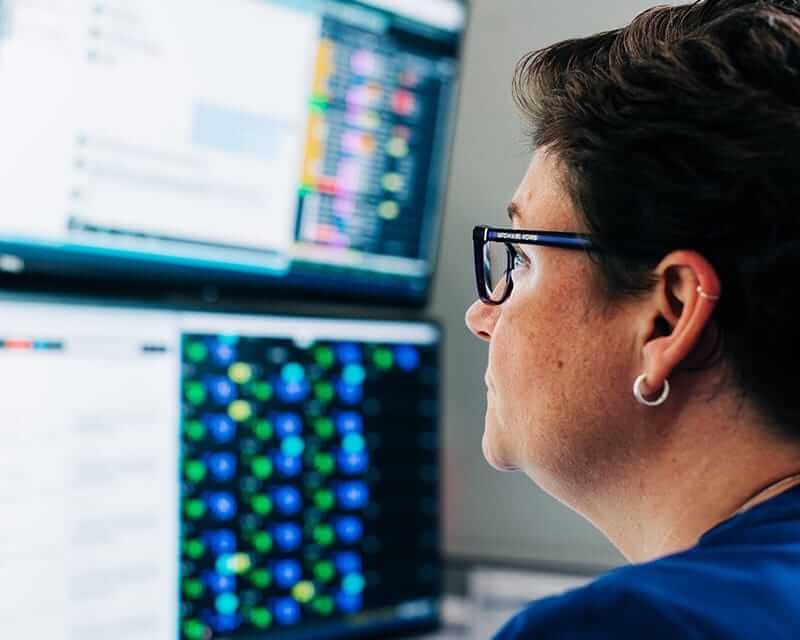 A woman looking at data on two computer monitors. 