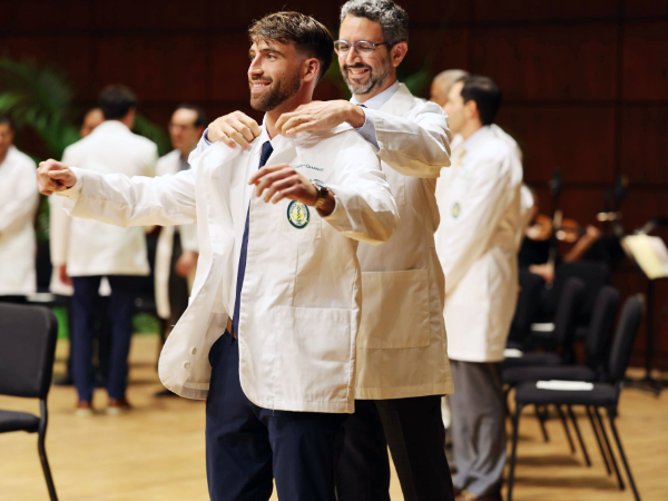 Male dental student being coated by faculty member on stage during White Coat Ceremony